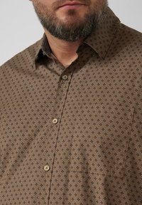 Brown patterned shirt with a button-down collar, featuring a small pocket and tan buttons. The fabric has a textured, subtle geometric design.