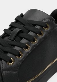 Sneaker in pelle nera con occhielli e lacci dorati, caratterizzato da una superficie testurizzata e un accento dorato lungo la suola.