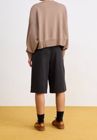 Brauner, verkürzter Hoodie, schwarze Shorts, schwarze Socken, braune Sneakers. Schlichtes Design, weiche Textur, Shorts reichen bis zur Mitte des Oberschenkels, lässige Passform.