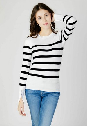 Zwart-wit gestreepte trui met lange mouwen, ronde halslijn en decoratieve knoopaccenten op de manchetten. Een paar blauwe jeans zichtbaar.