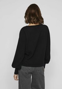 Pull noir à coupe ample, col rond et manches ballons longues ; associé à un jean gris délavé. La texture semble douce et confortable.