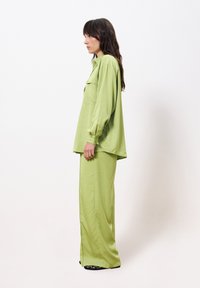 Groene, lichtgewicht blouse met een kraag en een voorzak, gecombineerd met bijpassende wijde broek. De stof is glad met een subtiele glans.
