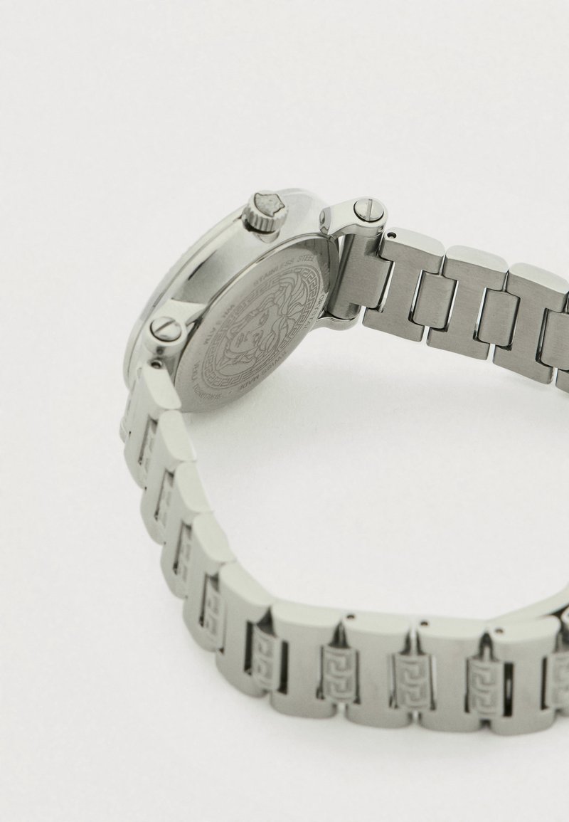 Silberne Armbanduhr aus Edelstahl mit rundem Gehäuse, strukturierter Rückseite und Gliederarmband mit gemustertem Design. Enthält eine Krone bei 2 Uhr.