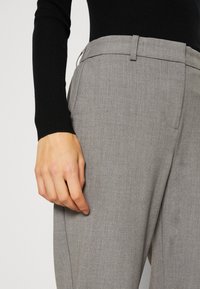 Pantalon gris en tissu texturé. Il présente un devant plat et des poches latérales, avec une passants de ceinture à la taille.