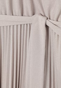 Abito in tessuto beige chiaro con design plissettato e vita legata. Il materiale ha una leggera lucentezza e una consistenza liscia.