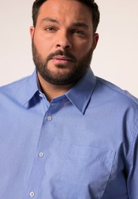 Lichtblauw overhemd met puntige kraag, borstzak en gestructureerde stof, voorzien van kleine knopen en een relaxte pasvorm.