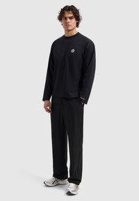 Black long-sleeve shirt with a round neckline and embroidered logo, paired with black pants and light-colored athletic shoes.