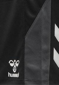 Svart och grå sportig tyg med en Hummel-logotyp och ett chevronmönster i vitt, som framhäver en texturerad yta och en elegant design.