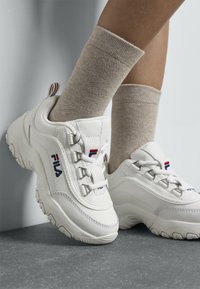 Baskets de sport blanches avec bout arrondi, tige en cuir texturé, accents de logo rouges et bleus contrastants, et design à lacets à l'avant.