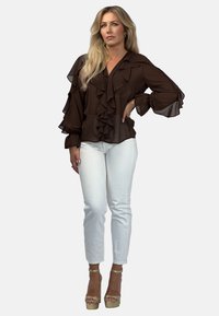 Brązowa bluzka z falbanami, z przejrzystymi rękawami, dekoltem w serek, połączona z białymi dopasowanymi dżinsami i złotymi platformami. Czyste, nowoczesne detale projektu.