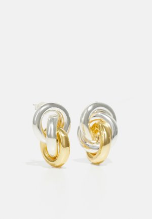 Divi savienojami auskari ar spīdīgiem sudraba un zelta posmiem, ar gludu, noapaļotu dizainu un bezšuvju tekstūru.