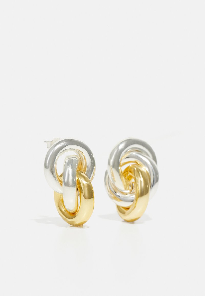 Deux boucles d'oreilles entrelacées avec des maillons en argent et en or brillants, au design lisse et arrondi, avec une texture sans couture.