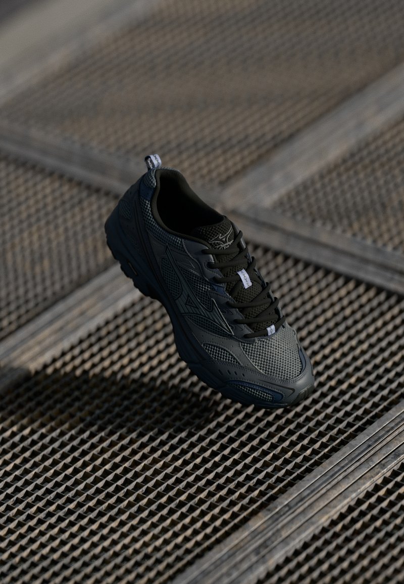 Črne atletske čevlje z mrežasto zasnovo, gumijastim podplatom in sistemom za vezanje. Imajo zanko za lažje obuvanje in teksturirano zgornji del za zračnost in oporo.