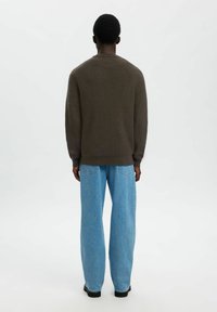 Rjav rebrast pulover z dolgimi rokavi, v kombinaciji s svetlo modrimi širokimi hlačami. Outfit ima sproščen kroj in minimalne detajle.