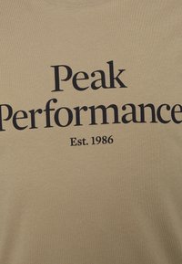 Tanfarvet bomuld T-shirt med mørkeblå tekst: "Peak Performance" med "Est. 1986" under. Blød tekstur, klassisk rund hals.
