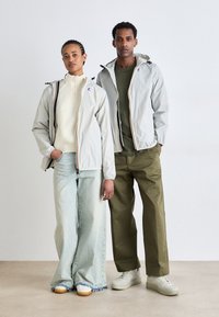 Light gray jackets with contrasting zipper details, worn over a white knit sweater and dark green shirt. Light blue wide-leg jeans, olive green pants.