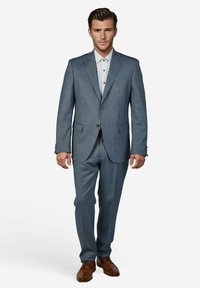 Hellgrauer Anzug mit strukturierter Stoffqualität, Ein-Knopf-Verschluss, Revers mit Kerbe und passende Hosen. Braune Anzugschuhe. Weißes Hemd mit Muster darunter.