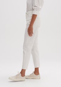 Vita jeansbyxor i denim med en figursydd design och avsmalnande ben längst ner, kombinerade med ljusa sneakers i canvas. Mjuk textur och minimala sömnadsdetaljer.