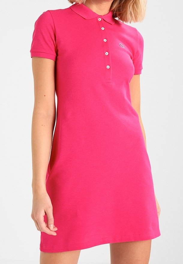 Femme portant une robe polo à manches courtes rose vif, avec des boutons et un petit logo sur la poitrine.