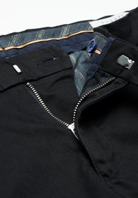 Ciemne spodnie z otwartym srebrnym zamkiem błyskawicznym, niebieskim guzikiem i metalowym zapięciem, odsłaniające wzorzystą podszewkę w pasie.