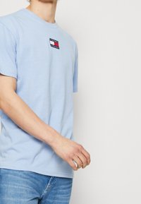 Ljust blå bomull t-shirt med korta ärmar, med en liten rektangulär logopatch i marinblått, vitt och rött på bröstet.