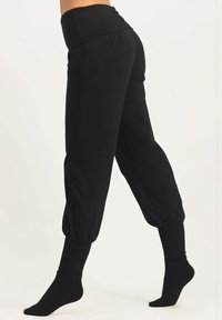 Svarta byxor med en bred, vikad midja, åtsittande muddar och en lös, avsmalnande form. Tillverkade av mjukt tyg med en jämn yta.