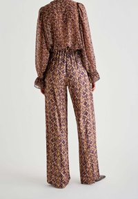 Brun mønster outfit med en bluse med puffærmer og brede bukser. Stoffet er let og har en glat tekstur med kontrasterende lilla accenter.