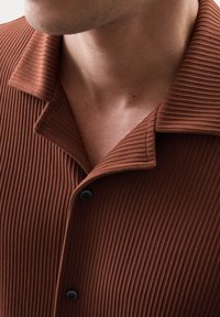 Chemise marron à côtes présentant un petit col et des boutons noirs, mettant en valeur un tissu texturé avec des nervures verticales.