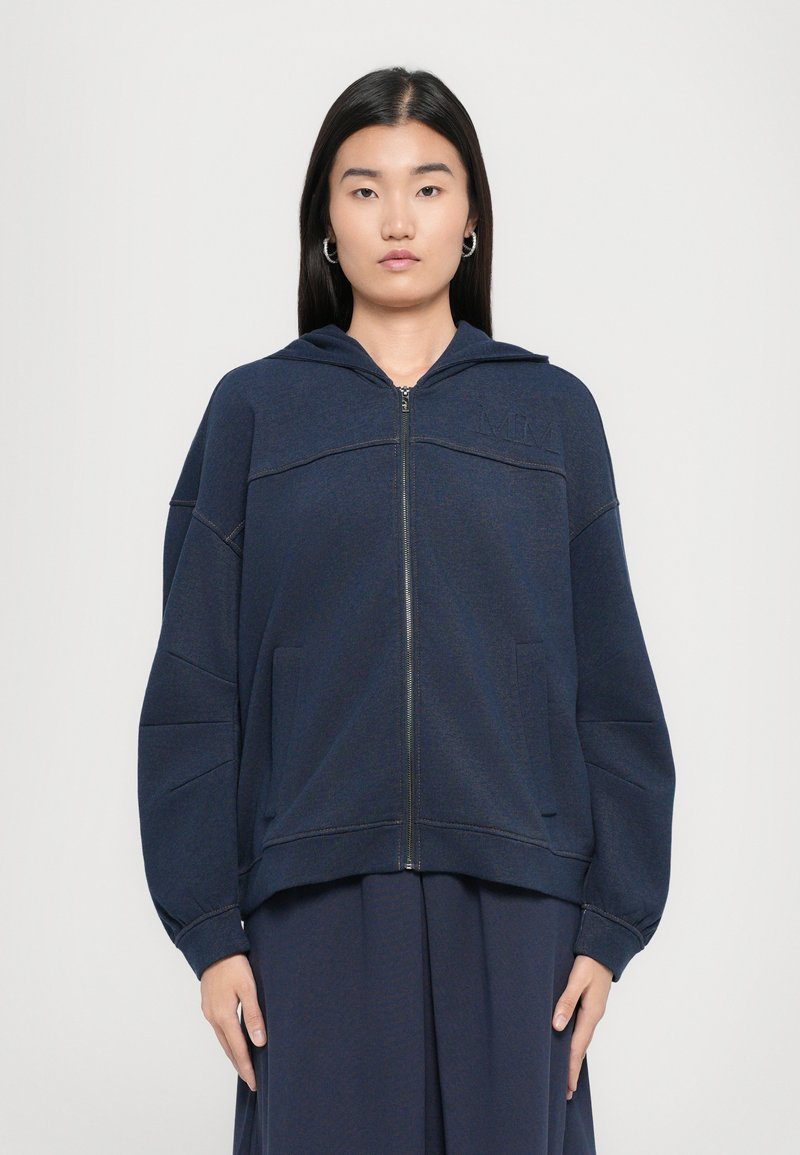 Felpa con zip color navy realizzata in tessuto morbido, caratterizzata da una vestibilità ampia, tasche a marsupio e un cappuccio con cordino e cuciture tono su tono.