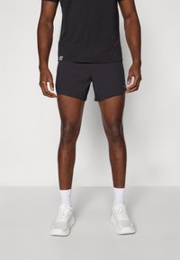 Black athletic shorts in a lightweight fabric, featuring a fitted design. Paired with a black t-shirt and white athletic shoes.