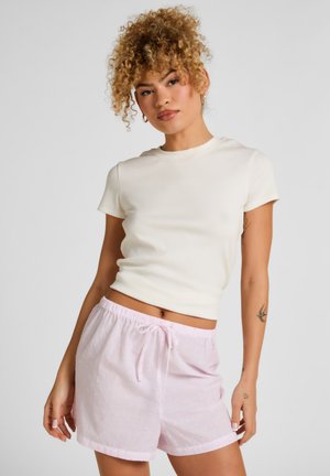 Lichtbeige nauwsluitend T-shirt en roze gebloemde korte broek met een elastische tailleband en trekkoord. De korte broek heeft kleine, verspreide stippen.
