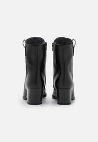 Zwarte leren enkellaarzen met een gestructureerd oppervlak, medium hoogte blokhak en ritssluiting aan de achterkant. Gevoerd met zacht grijs stof.