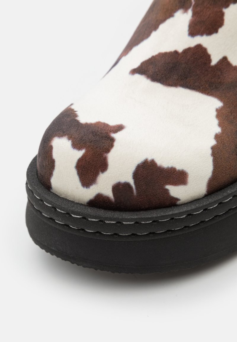 Cowprint-Stiefel mit einem weichen, strukturierten Obermaterial in Weiß und Braun. Verfügt über eine schwarze, klobige Sohle mit sichtbaren Nähdetails.