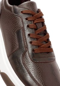 Primer plano de una zapatilla de cuero texturizado marrón oscuro con cordones a juego y una suela de goma blanca.