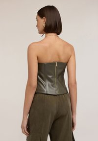 Top corsetto senza spalline in verde oliva, realizzato in materiale lucido, con zip sul retro. Abbinato a pantaloni larghi in verde oliva.