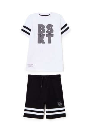 Camiseta blanca de manga corta con texto negro "BSKT" y rayas en las mangas, combinada con pantalones cortos negros con cordón que presentan rayas blancas y texto a juego.