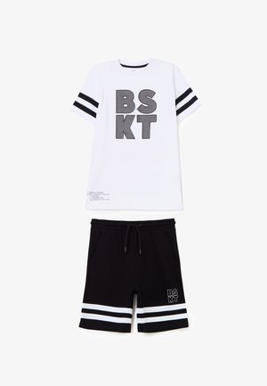Witte T-shirt met korte mouwen, zwarte tekst "BSKT" en strepen op de mouwen, gecombineerd met zwarte shorts met trekkoord, witte strepen en bijpassende tekst.