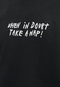 Zwarte stof met wit geborduurde tekst met hoofdletters: "WHEN IN DOUBT TAKE A NAP!"