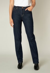 Donkerblauwe denim jeans met een rechte pasvorm, voorzakken en subtiele gouden stiksels. Gedragen met een witte top en zwarte enkellaarsjes.