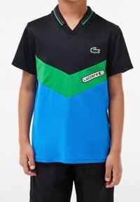 Black, green, and blue polo shirt made of breathable fabric; features a V-neck, color-block design, and Lacoste logo on the chest.