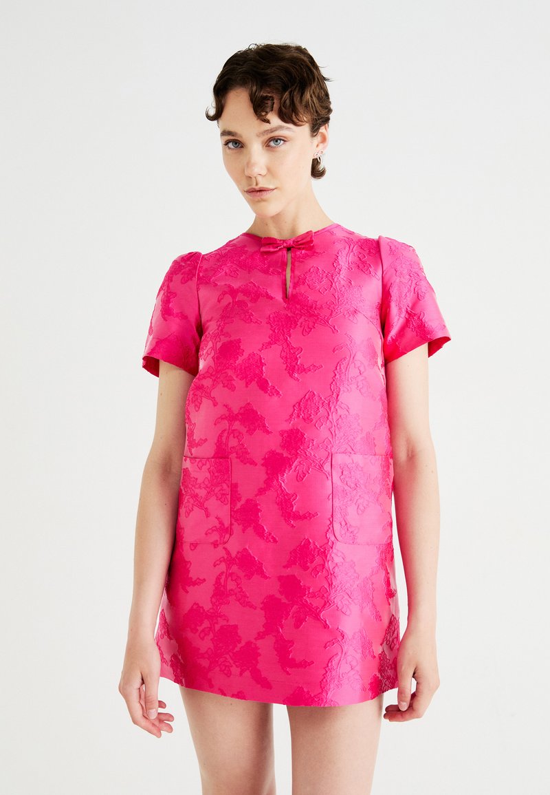 Kurzärmeliges pinkes Kleid mit geprägtem Blumenmuster. Es hat einen runden Ausschnitt, einen Schlüssellochverschluss und zwei aufgesetzte Taschen auf der Vorderseite.