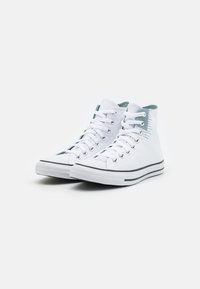 Bílé plátěné sneakersy s vysokým profilem a šedými akcenty, černou gumovou podrážkou a kulatou špičkou. Obsahují pět kovových očíček a ploché bílé tkaničky.