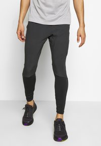 Leggings deportivos negros con diseño ajustado, tela texturizada y acentos en bloques de color. Combinados con zapatillas negras con detalles morados.