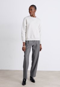 Lys grå hettegenser med rund hals, kombinert med mørkegrå dressbukser. Antrekket har en smidig tekstur og avslappet passform.