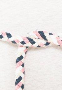 Spleciony sznurek z różowymi, granatowymi, białymi i kremowymi wplecionymi wzorami, związany w węzeł, na tle jasnoszarego teksturowego tła.