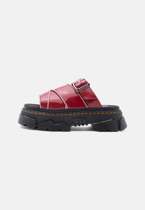 Κόκκινο γυαλιστερό δερμάτινο σανδάλι με ανοιχτό δάχτυλο, παχύ μαύρο σχεδιασμένο πέλμα και ρυθμιζόμενη λουρί με αγκράφα σε λευκό φόντο.