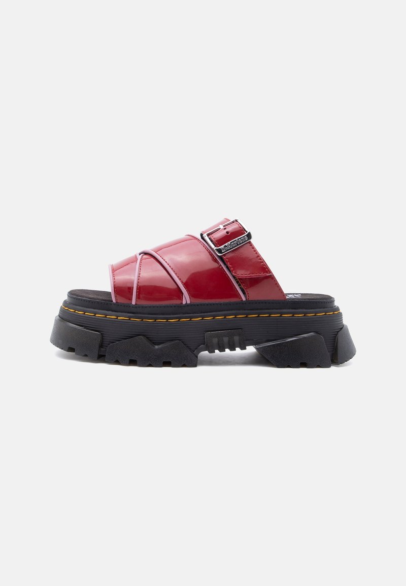 Κόκκινο γυαλιστερό δερμάτινο σανδάλι με ανοιχτό δάχτυλο, παχύ μαύρο σχεδιασμένο πέλμα και ρυθμιζόμενη λουρί με αγκράφα σε λευκό φόντο.