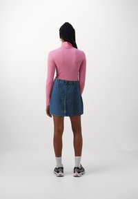 Långärmad rosa topp i kombination med en blå denim minikjol, svarta sneakers och vita ankelsockor. Enkel, figurnära design utan mönster.