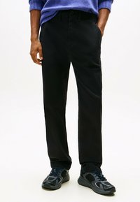 Pantaloni neri con un design a gamba dritta, realizzati in tessuto morbido. Abbinati a scarpe da ginnastica nere con dettagli in rete e lacci.