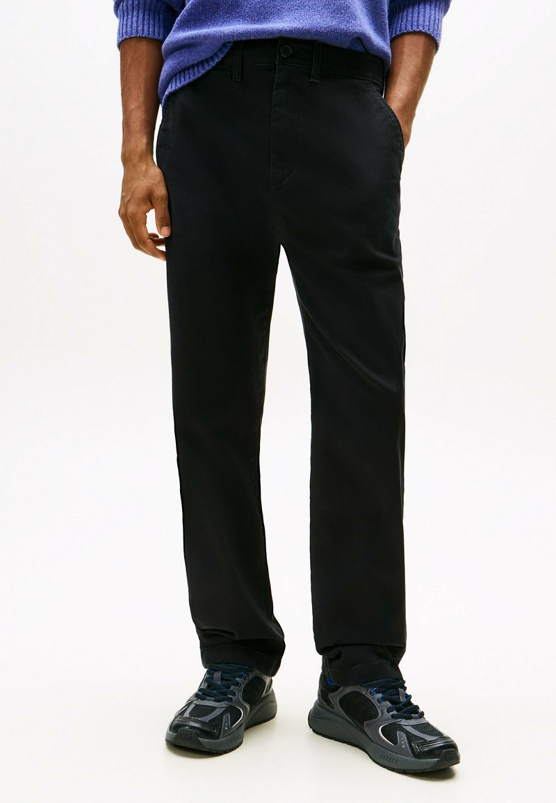 Pantalon noir au design droit, fabriqué à partir d'un tissu lisse. Associé à des chaussures de sport noires avec des accents en maille et des lacets.